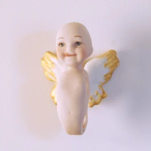 Bambolina angioletto in porcellana biscuit con sorriso birichino, linguetta di fuori e ali bianche con punte dorate.
