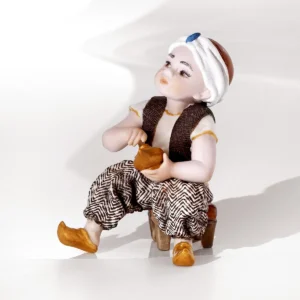 Statua in porcellana di Aladino con turbante e babbucce dorate, seduto su uno sgabello rosso con lampada dorata.