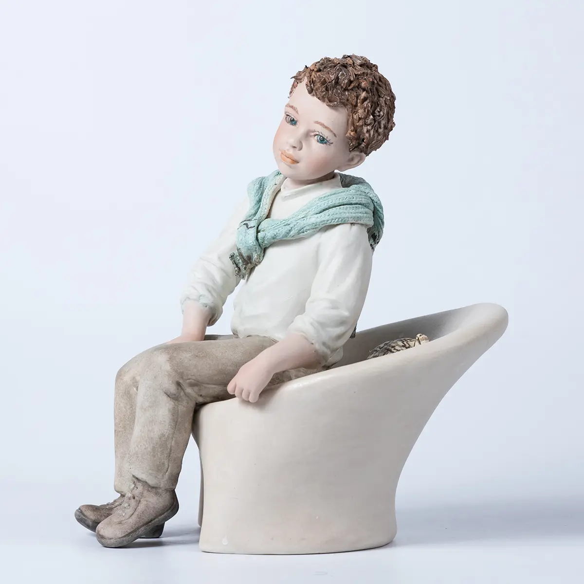 Figura in porcellana Alan, ragazzo seduto su poltrona bianca con camicia bianca e maglioncino azzurro sulle spalle.