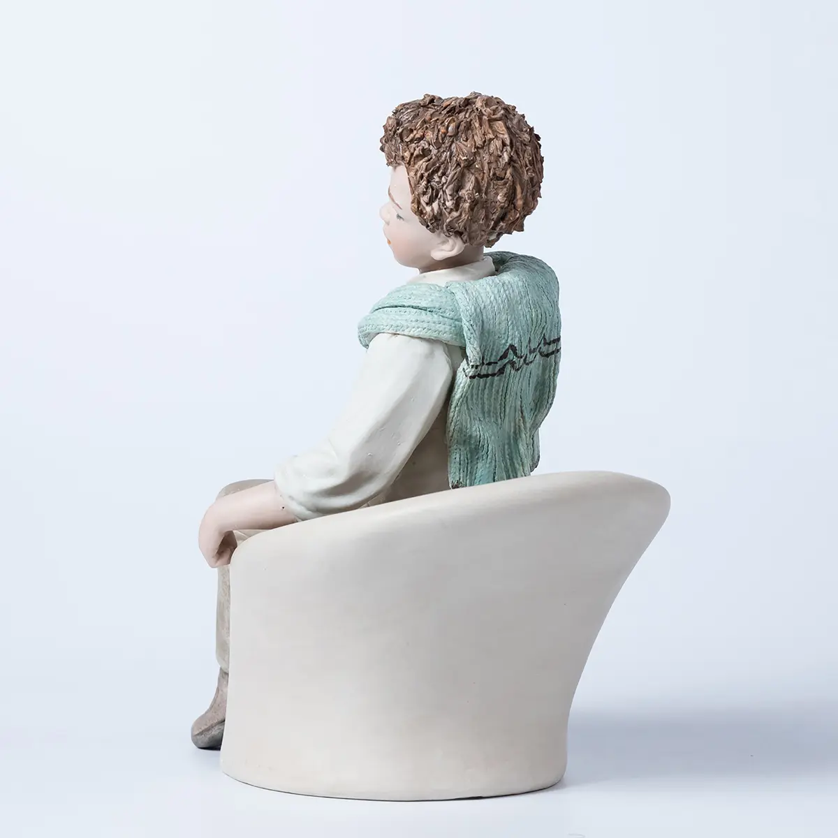 Statua in porcellana di Alan, ragazzo seduto su poltrona bianca con camicia e maglioncino azzurro sulle spalle.