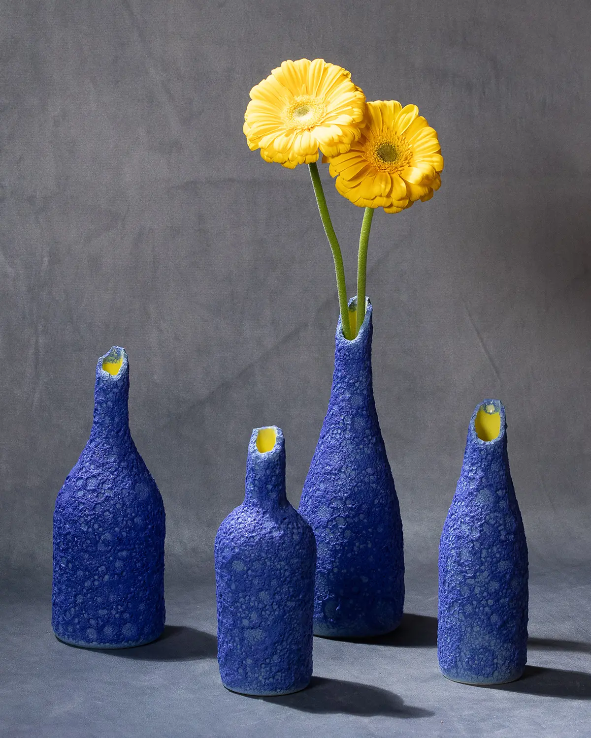 Bottiglie in porcellana Aphrós in smalto blu dal collo rotto con dei fiori gialli
