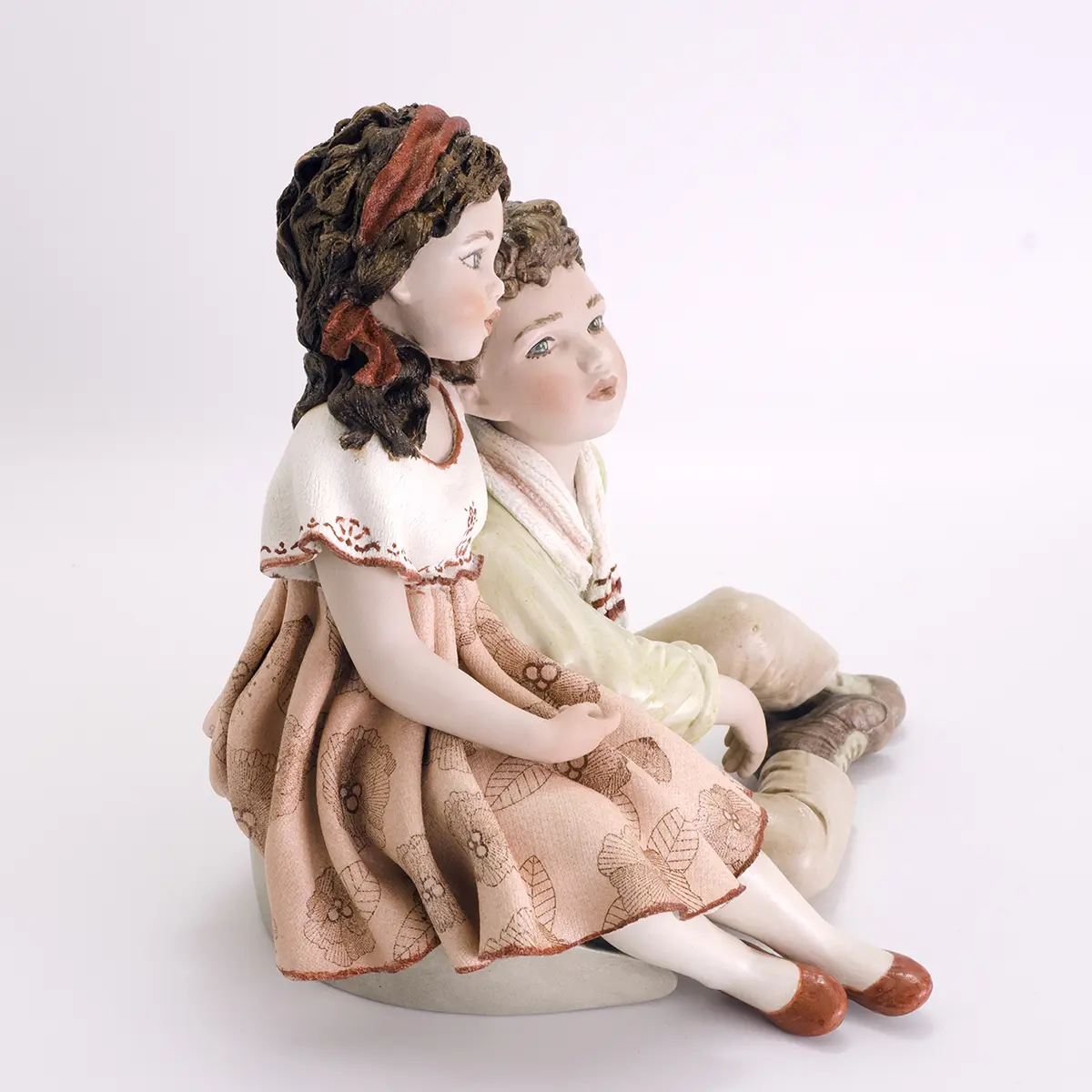 Statua in porcellana di coppia di ragazzi abbracciati, lei in abito rosa a fiori e lui in camicia verde e pantaloni beige.