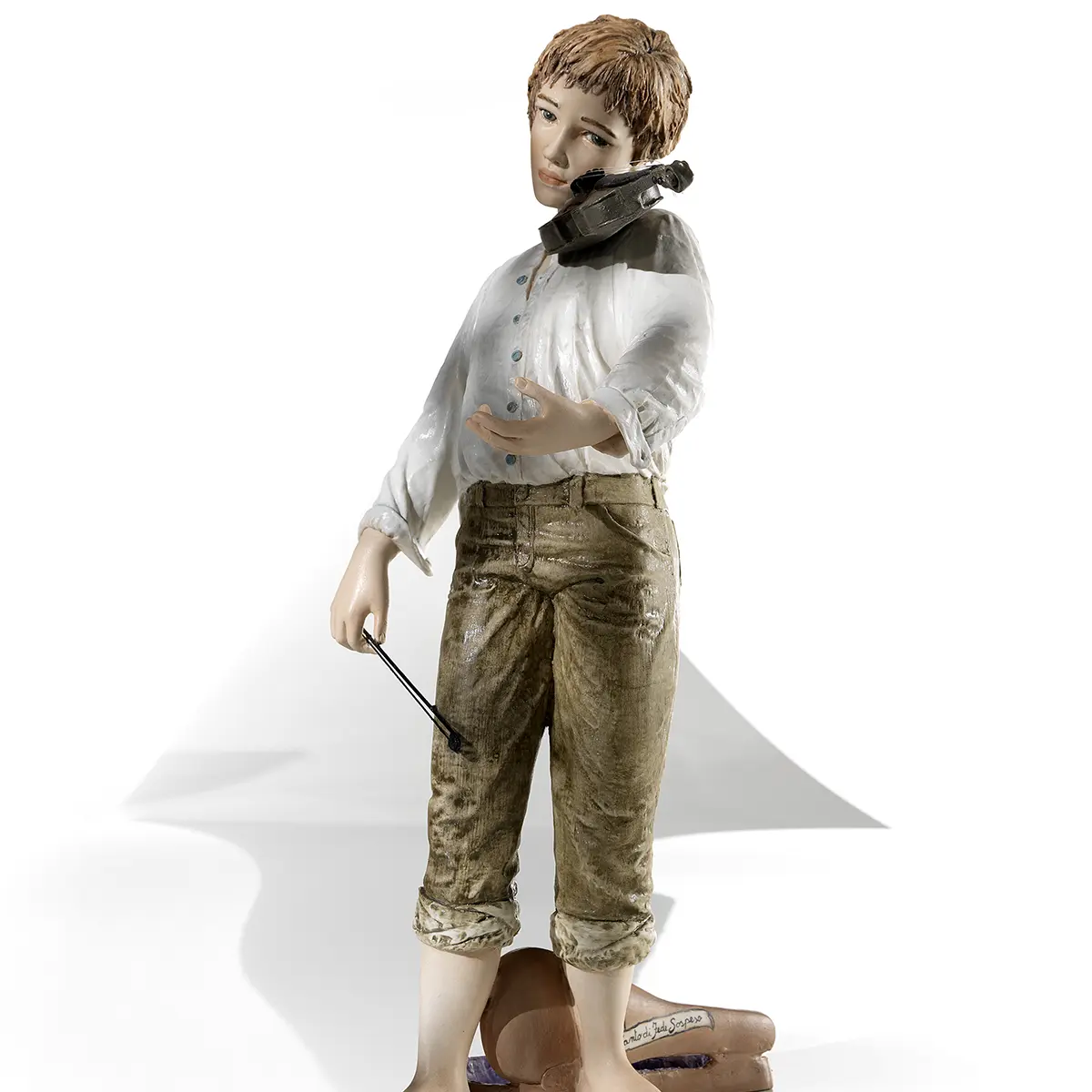 Statua in porcellana di ragazzo con violino, camicia bianca e pantaloni verde senape in piedi davanti alla custodia.