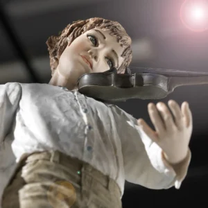 Statua in porcellana di ragazzo violinista in camicia bianca e pantaloni verde senape davanti alla custodia del violino.