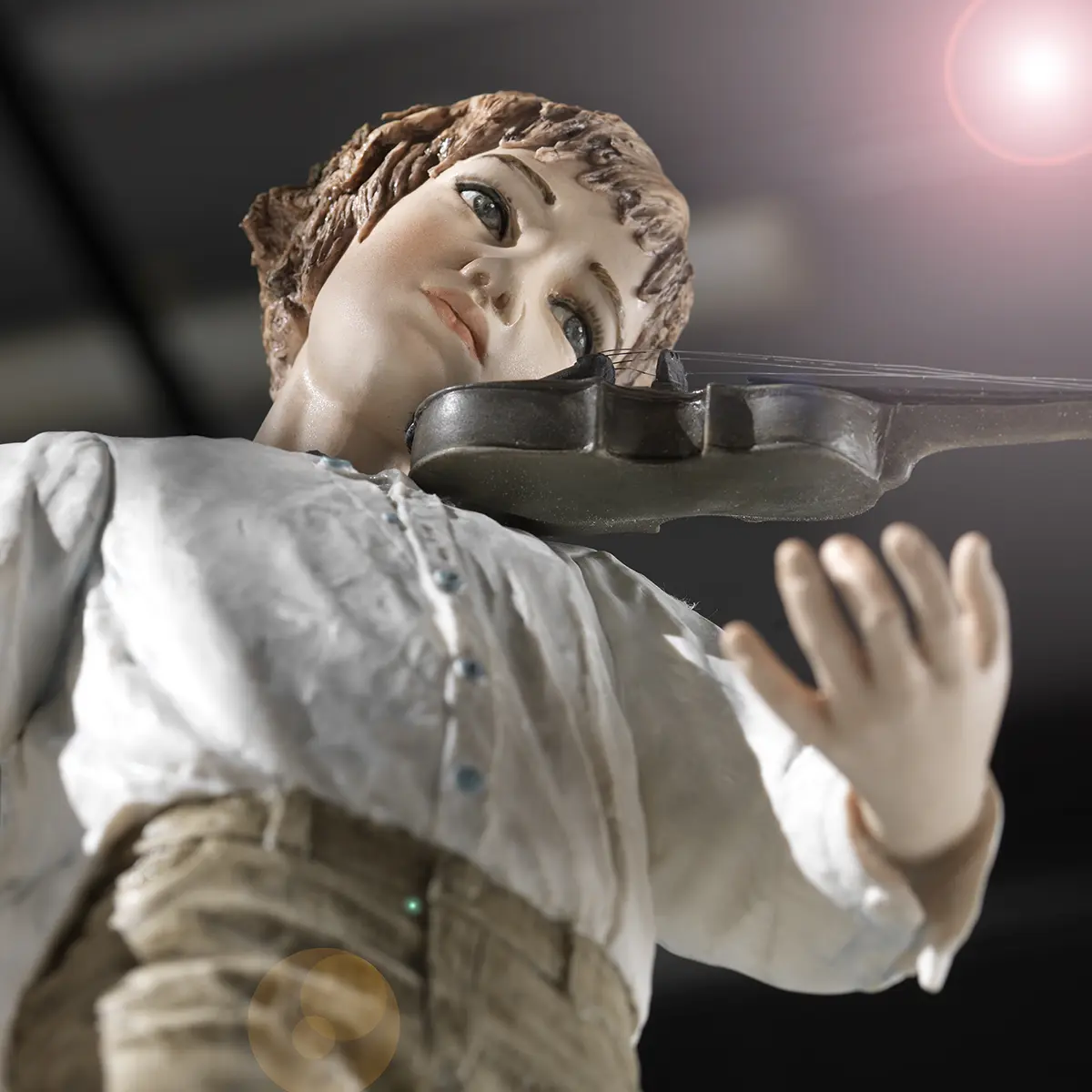 Statua in porcellana di ragazzo violinista in camicia bianca e pantaloni verde senape davanti alla custodia del violino.