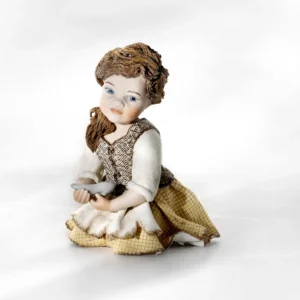 Statua in porcellana di Cenerentola in ginocchio con la scarpetta di cristallo, gonna a quadretti e grembiule bianco.