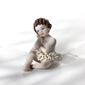 Statua in porcellana di bimba ballerina in tutù di pizzo, seduta a terra con viso sulla mano e fiocco nei capelli corti.