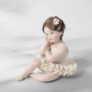 Statua in porcellana di bimba ballerina in tutù di pizzo, seduta a terra col viso sulla mano e fiocco tra i capelli corti.