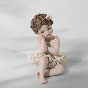 Statua in porcellana di bimba ballerina in tutù di pizzo, seduta a terra con viso su una mano e capelli corti con fiocco.