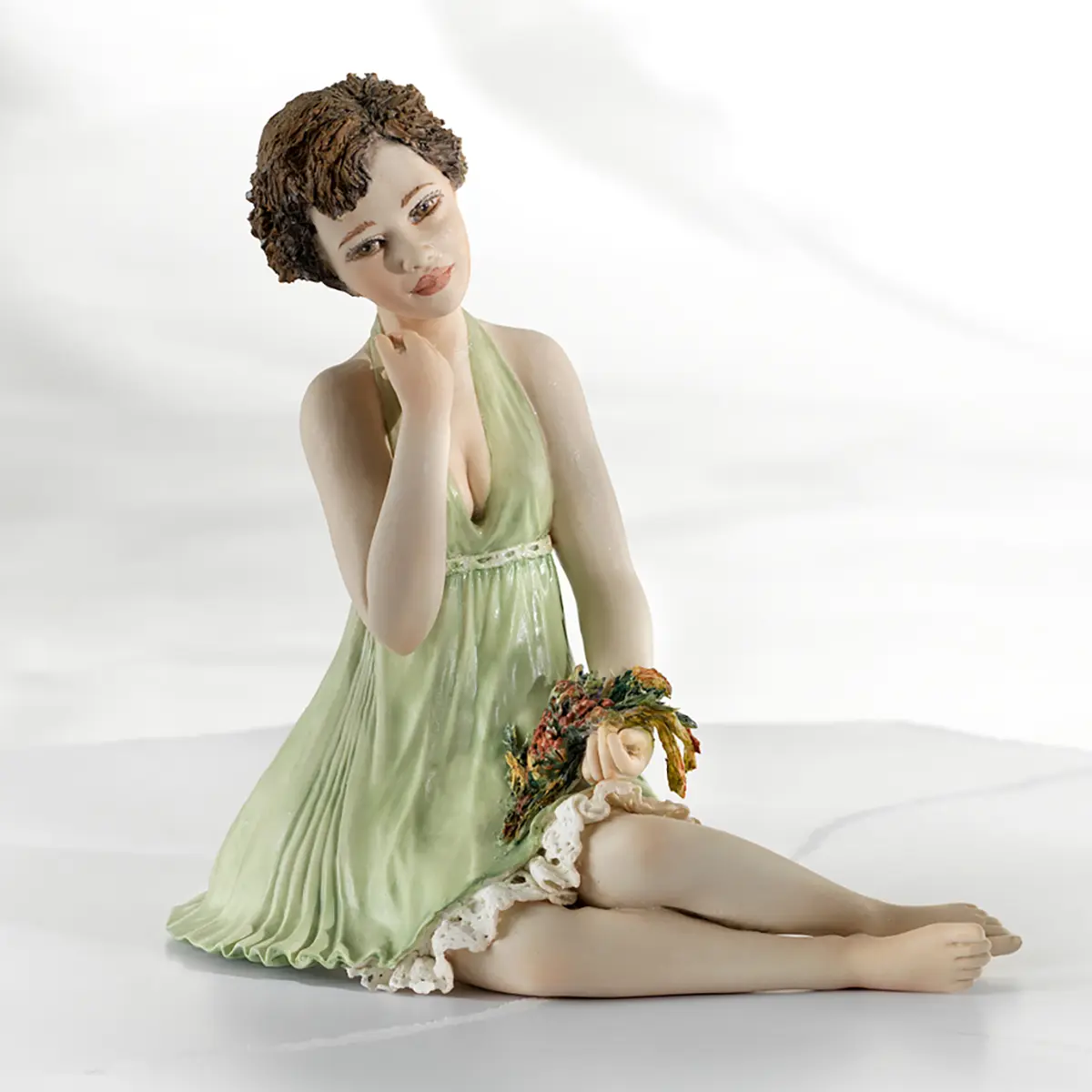 Statua in porcellana di donna seduta con mazzo di fiori, abito verde primavera, sottogonna in pizzo e capelli corti.