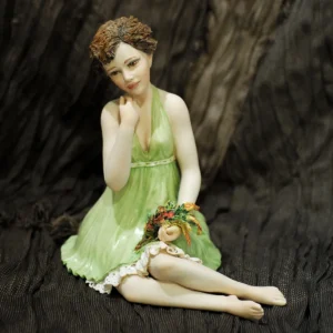 Statua in porcellana con donna seduta, mazzo di fiori, abito verde primavera e sottogonna in pizzo.
