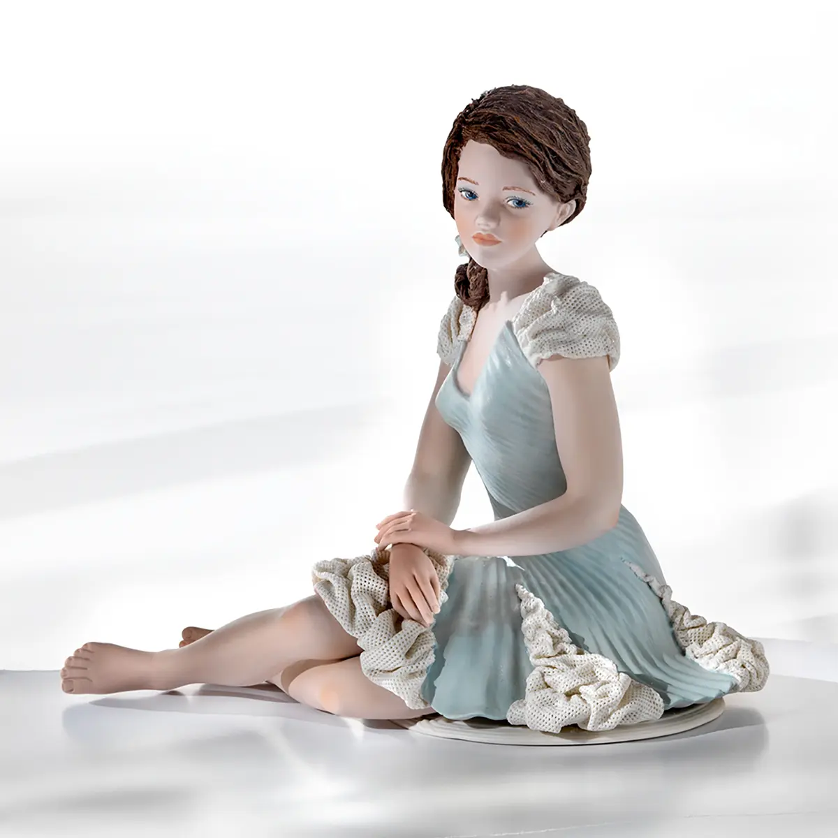 Statua in porcellana di donna seduta in elegante abito color Tiffany con inserti in tulle e fiocco nei capelli.