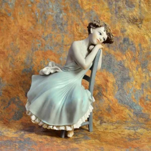 Statua in porcellana di giovane donna in lungo abito azzurro e tulle bianco, seduta su sedia turchese.
