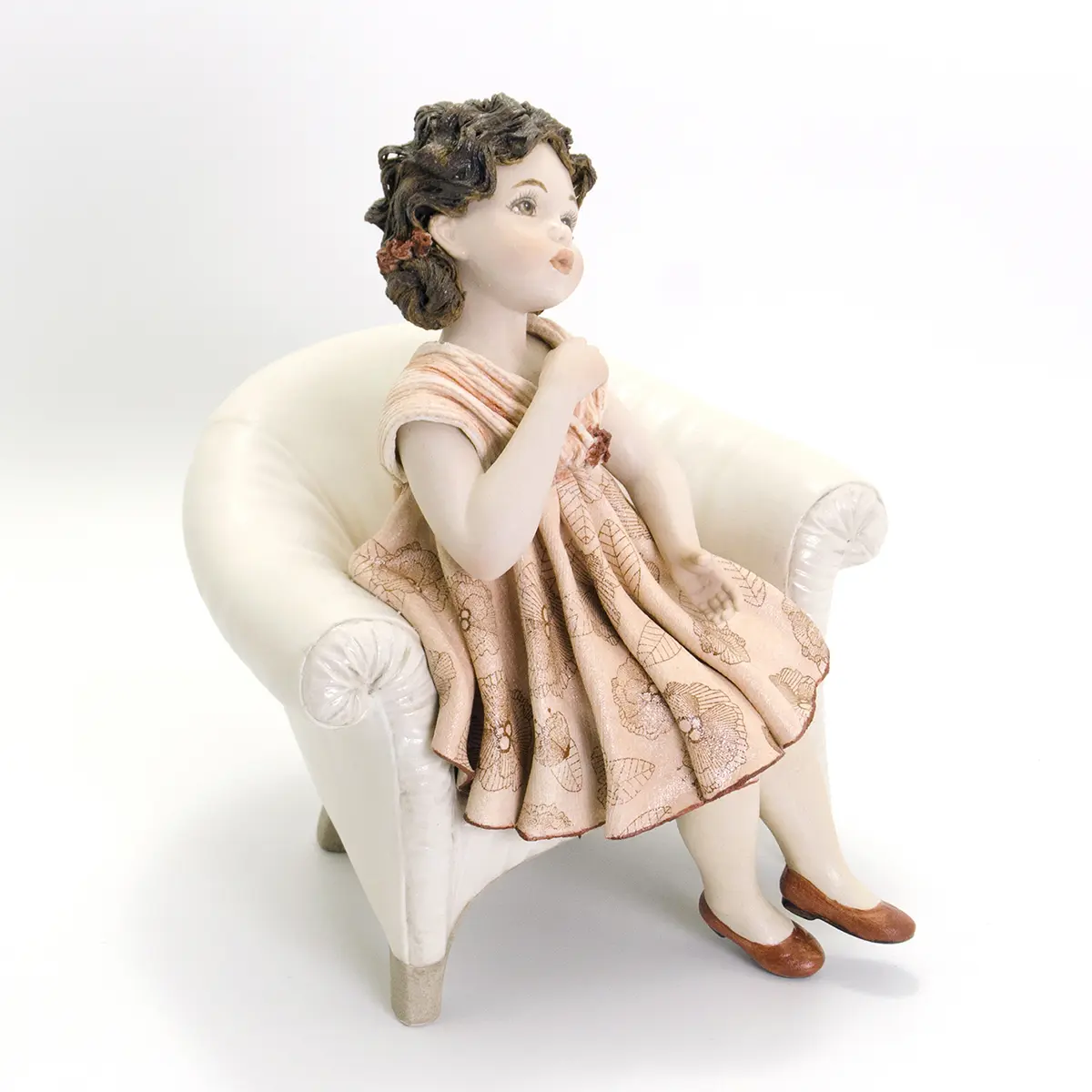 Statua in porcellana con ragazza seduta su poltrona bianca in abito rosa a fiori rossi e ballerine rosse.