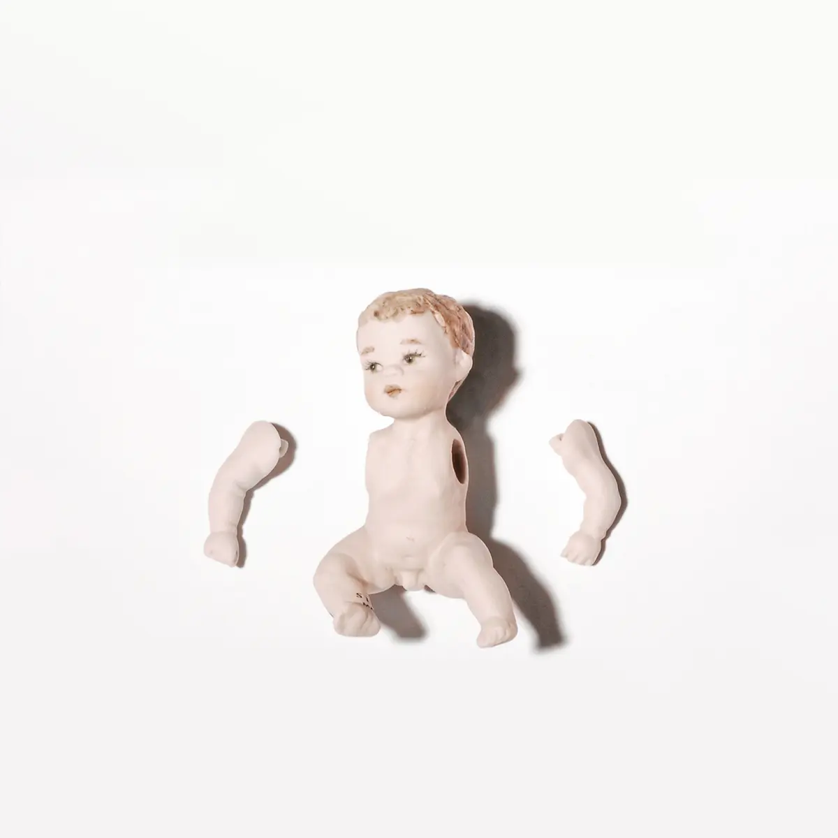 Bambolina in porcellana biscuit seduta a terra con braccia mobili e capelli corti castani.