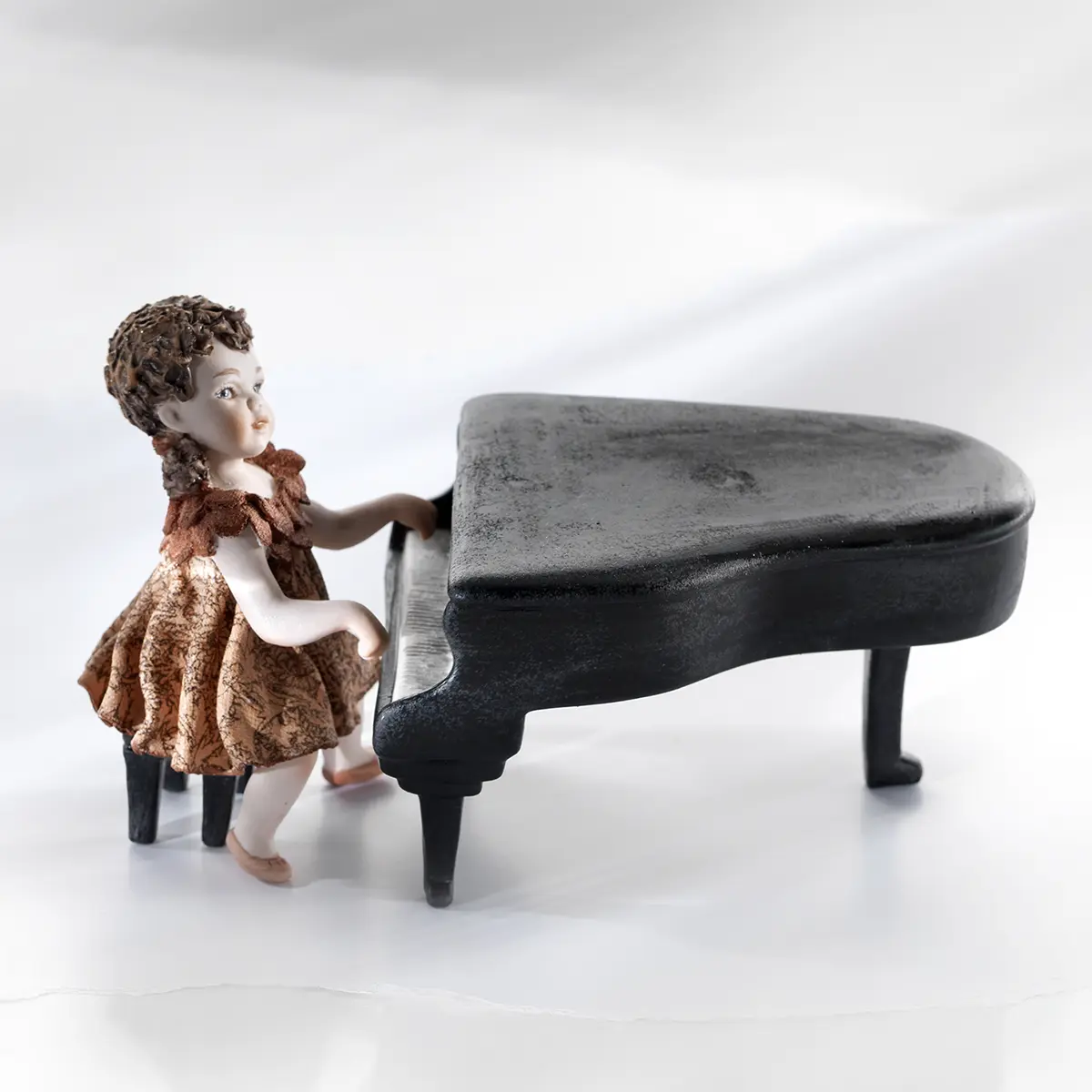 Statua in porcellana di una piccola pianista in abitino rosa che suona un pianoforte a coda nero.