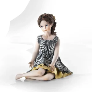 Statua in porcellana di ragazza seduta con abito bianco e nero, sottogonna e fiocco giallo tra i capelli.