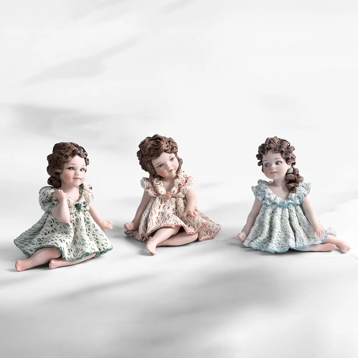 Statua in porcellana di bimba con abito in pizzo bianco e verde, fiocco sul petto e capelli raccolti in due chignon.