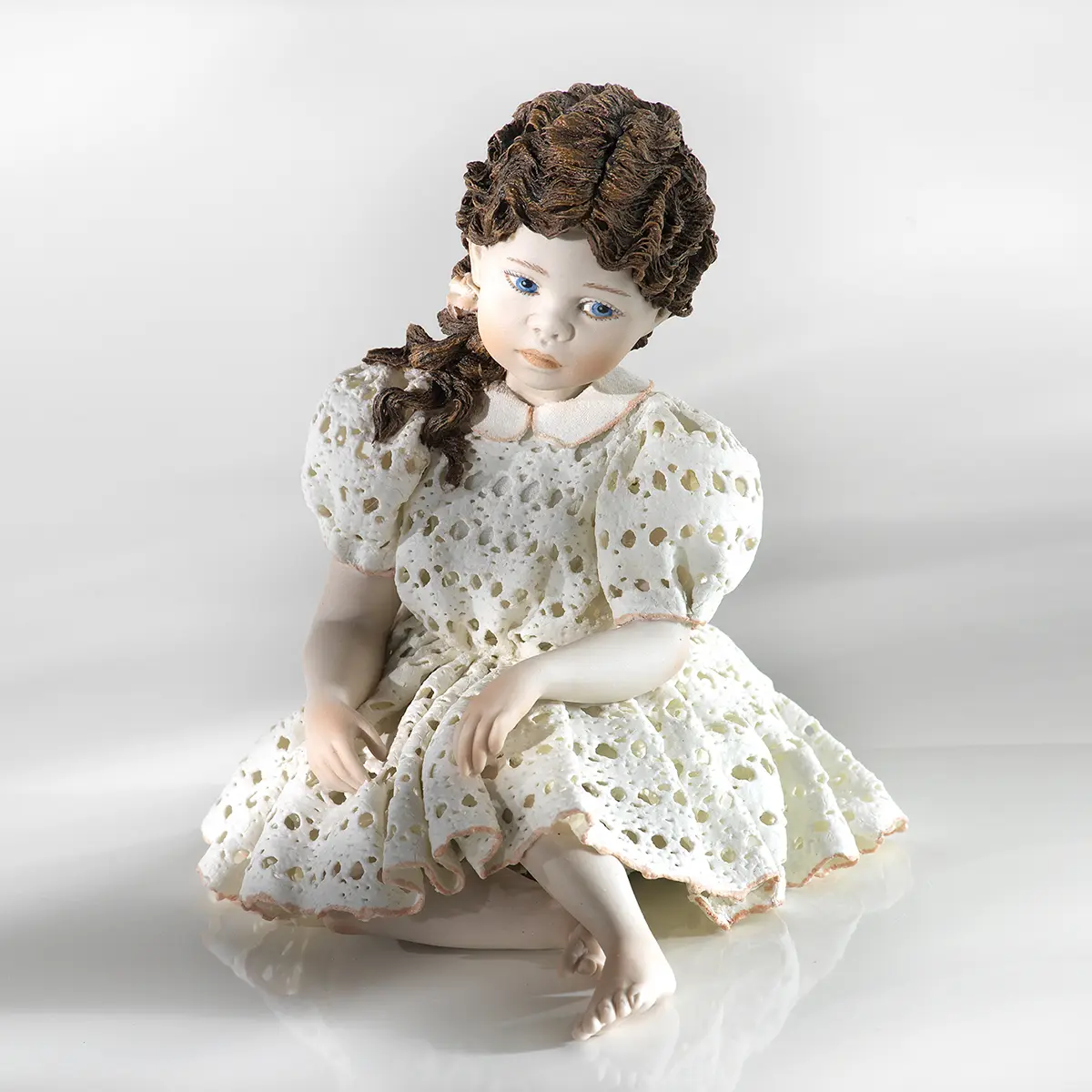 Statua in porcellana di ragazza seduta con abito in pizzo, maniche a palloncino, colletto bianco e capelli su una spalla.
