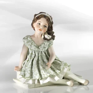 Statua in porcellana di ragazza con abito verde pastello e fascia bianca nei capelli, seduta su uno scalino.