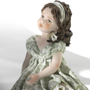 Statua in porcellana di ragazza con abito verde pastello e fascia bianca, seduta su uno scalino marmorizzato.