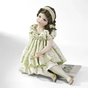 Statua in porcellana di ragazza in abito verde pastello, seduta su uno scalino con fascia bianca tra i capelli.