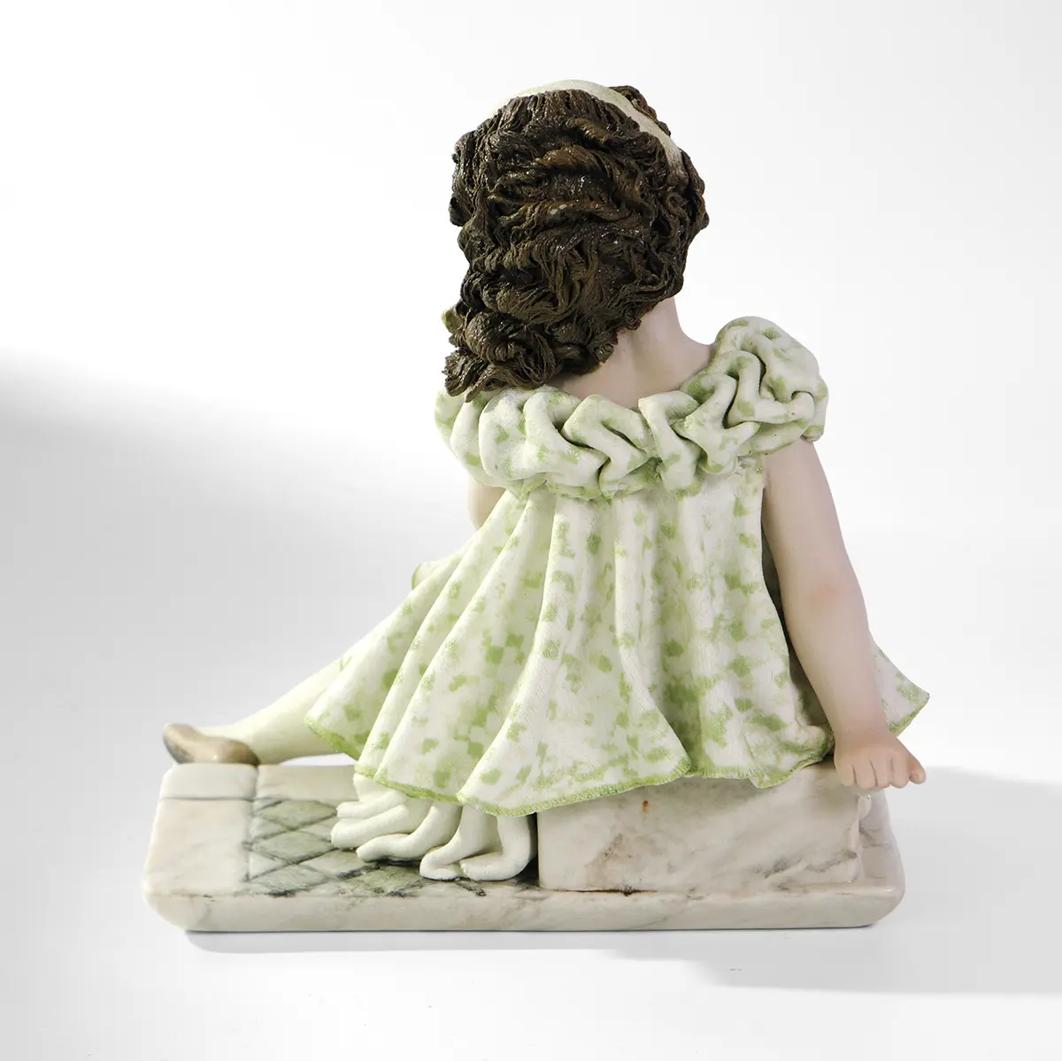 Statua in porcellana di ragazza in abito verde pastello seduta su uno scalino marmorizzato.