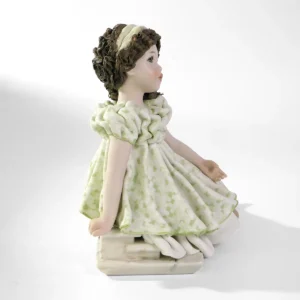 Statua in porcellana di ragazza in abito verde pastello seduta su uno scalino marmorizzato con fascia bianca nei capelli.
