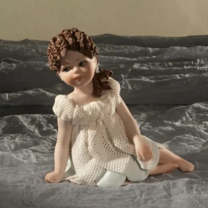 Statua in porcellana con bimba seduta a terra, abito in tulle a petali con sottogonna azzurra e capelli su una spalla.