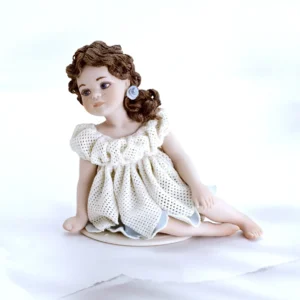 Statua in porcellana di bimba seduta con abito in tulle a petali, sottogonna azzurra e capelli su una spalla.