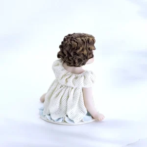 Statua in porcellana di bimba seduta con abito in tulle a petali, sottogonna azzurra e capelli su una spalla.