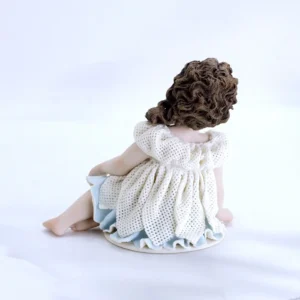 Statua in porcellana di bimba seduta in abito in tulle a petali, sottogonna azzurra e capelli su una spalla.