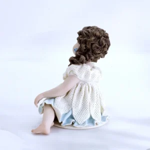 Statua in porcellana con bimba seduta in abito di tulle a petali, sottogonna azzurra e capelli su una spalla.