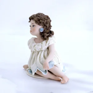 Statua in porcellana con bimba seduta in abito di tulle a petali, sottogonna azzurra e capelli su una spalla.