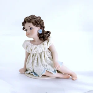 Statua in porcellana di bimba seduta con abitino in tulle a petali, sottogonna azzurra e capelli su una spalla.