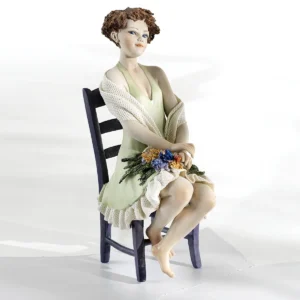 Statua in porcellana della Primavera: donna in abito verde pastello seduta su sedia glicine con mazzo di fiori in grembo.