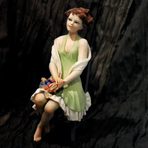 Statua in porcellana della Primavera: donna in abito verde pastello seduta con un mazzo di fiori colorati in grembo.