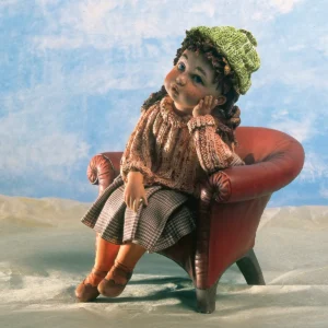 Statua in porcellana di bimba seduta su poltrona rossa con abiti invernali e berretto verde.