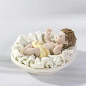 Statua in porcellana di Gesù Bambino in culla con panno crema e cuscino in tulle.