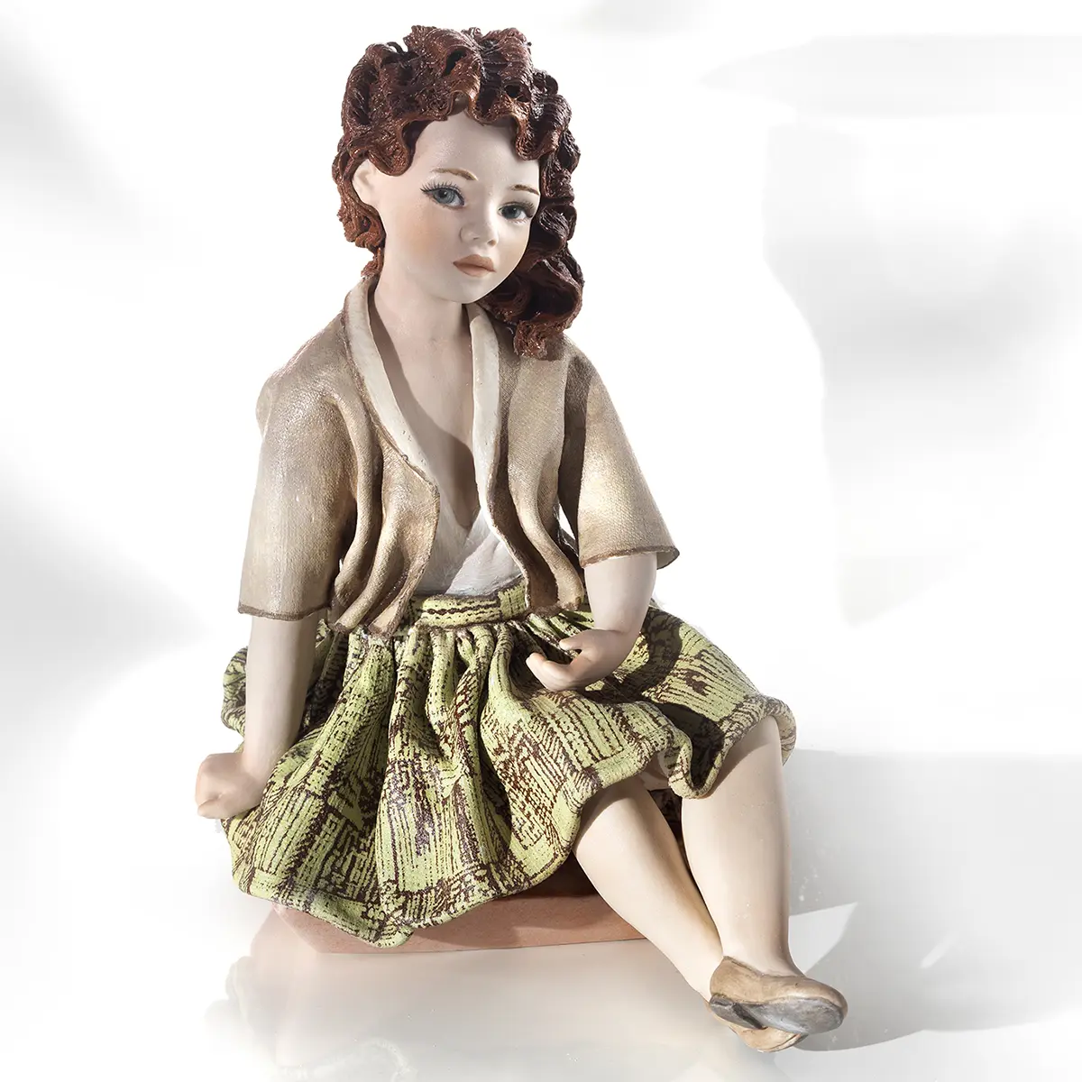 Statua in porcellana Giorgia 2020, ragazza con capelli rossi, gonna verde brillante e giacca nocciola, seduta a terra.