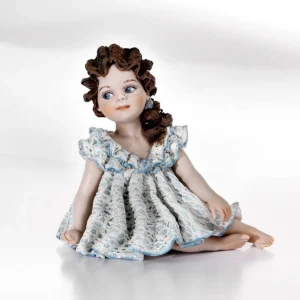 Statua in porcellana di bimba seduta a terra con abito in pizzo bianco e azzurro e coda con rosellina azzurra.