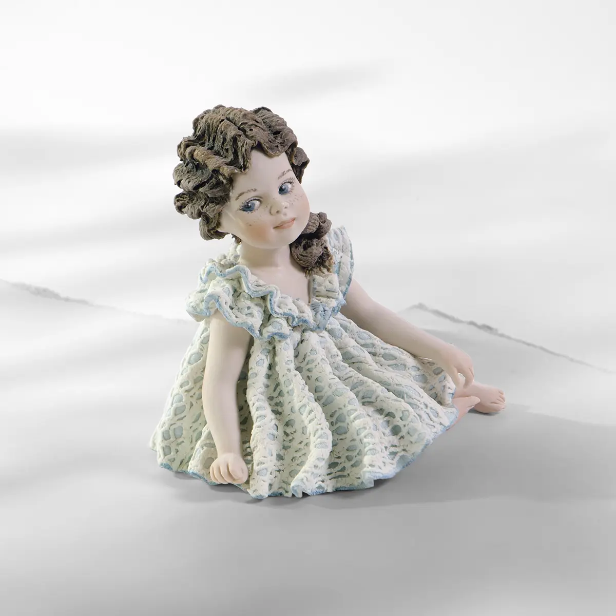 Statua in porcellana di bimba seduta con abito in pizzo bianco e azzurro e coda con rosellina.