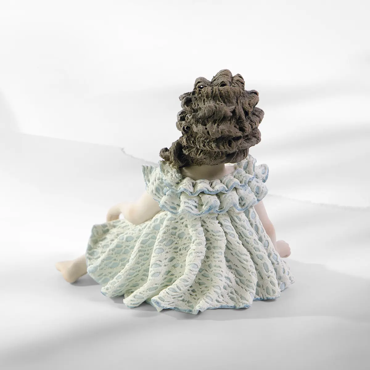 Statua in porcellana di bimba seduta con abito in pizzo bianco e azzurro, bavero a volants e coda con rosellina.