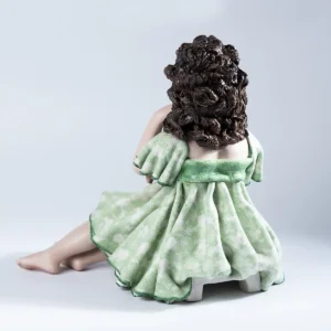Statua in porcellana di ragazza seduta su sgabello, con abito verde tè, bordi verde smeraldo e capelli sciolti.