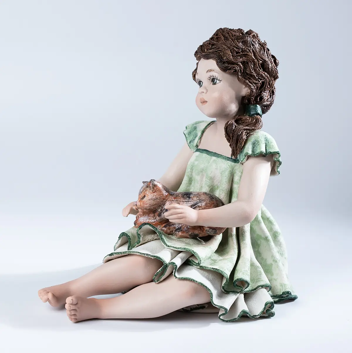 Statua in porcellana di ragazza pensierosa in abito verde tè e gatta in grembo.