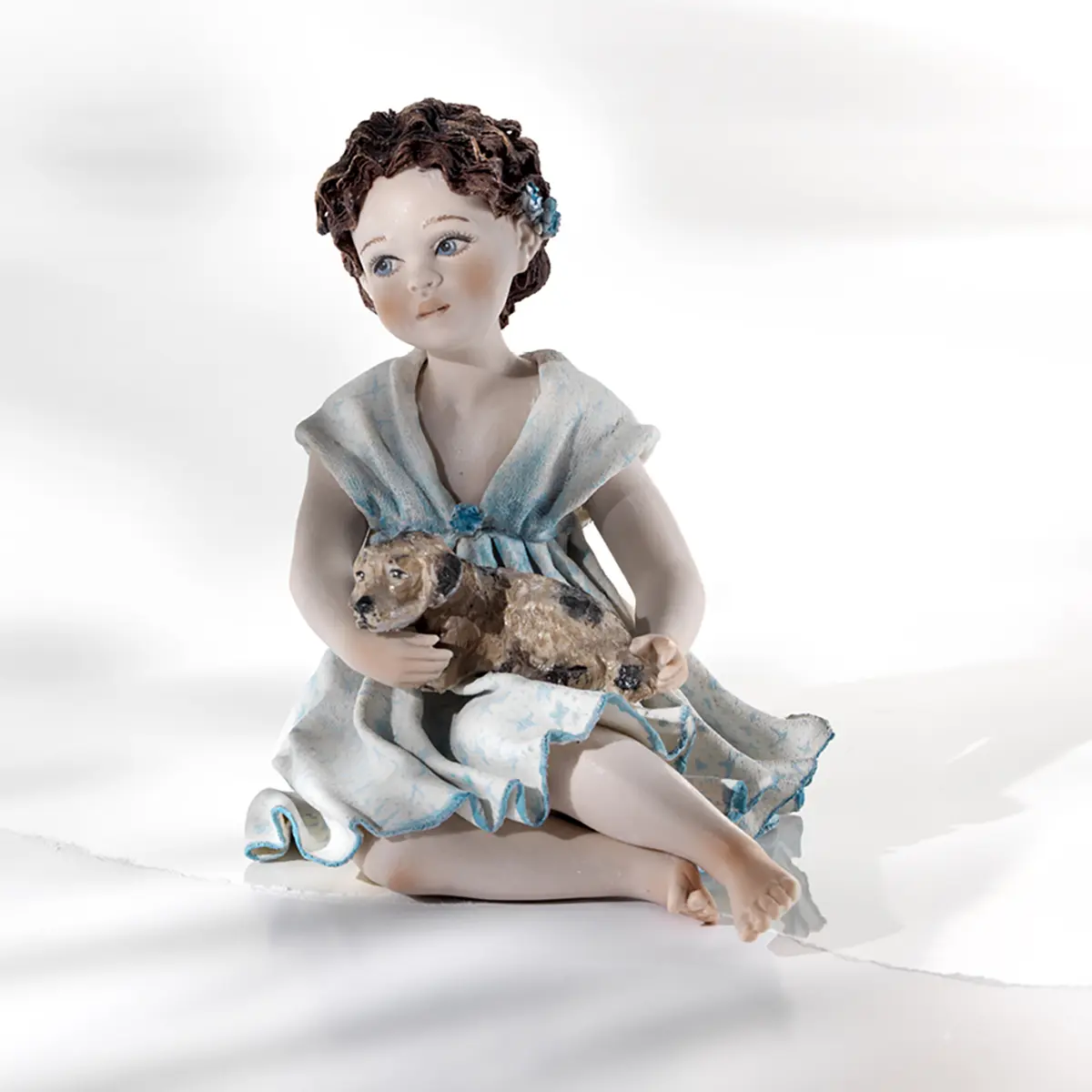 Statua in porcellana con ragazza in abito azzurro e cagnolino marroncino in braccio.