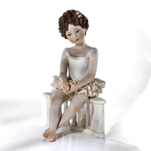 Statua in porcellana con ballerina in tutù di pizzo seduta su balaustra marmorizzata e fiocco bianco tra i capelli.