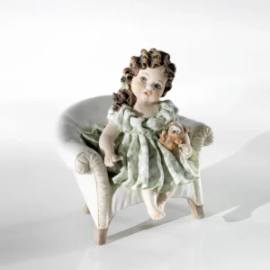 Statua in porcellana di Lisetta, bimba in abito verde pastello seduta su poltroncina bianca con il suo orsetto.