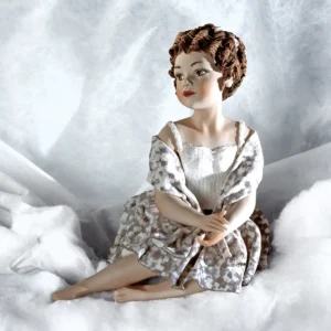Statua in porcellana di ragazza seduta a terra in gonna bianca e grigia con scialle e roselline tra i capelli.