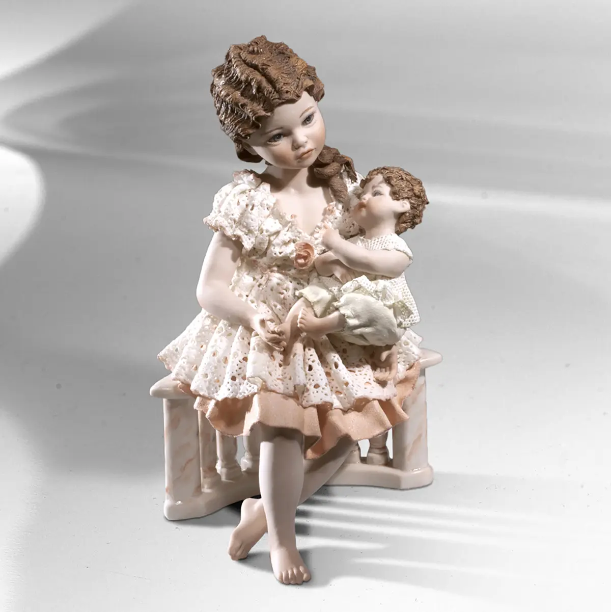 Statua in porcellana di giovane mamma in abito rosa che abbraccia il suo bimbo seduta su una balaustra.
